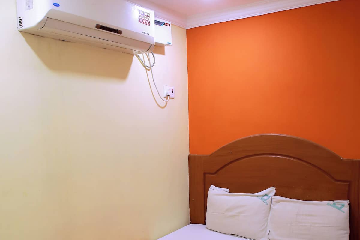 A single bed with an orange-striped bedspread, white pillows, and a white towel folded on the bed.