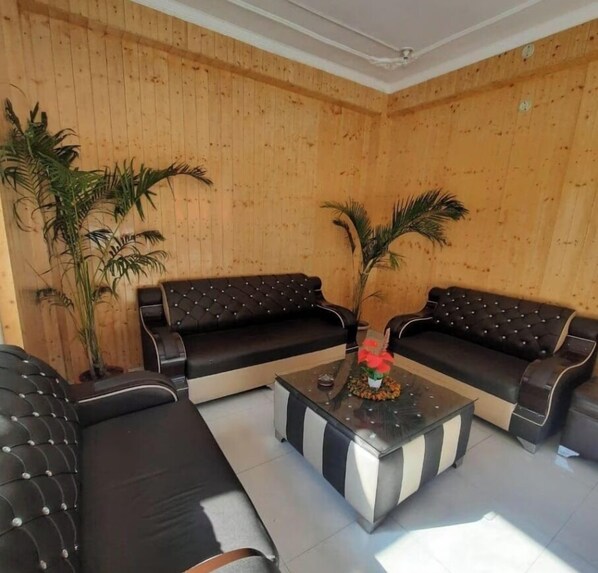 A room with two black leather sofas, a glass coffee table with a decorative centerpiece, and wooden panel walls. - Hotel Binog Breeze (Dhanaulti)