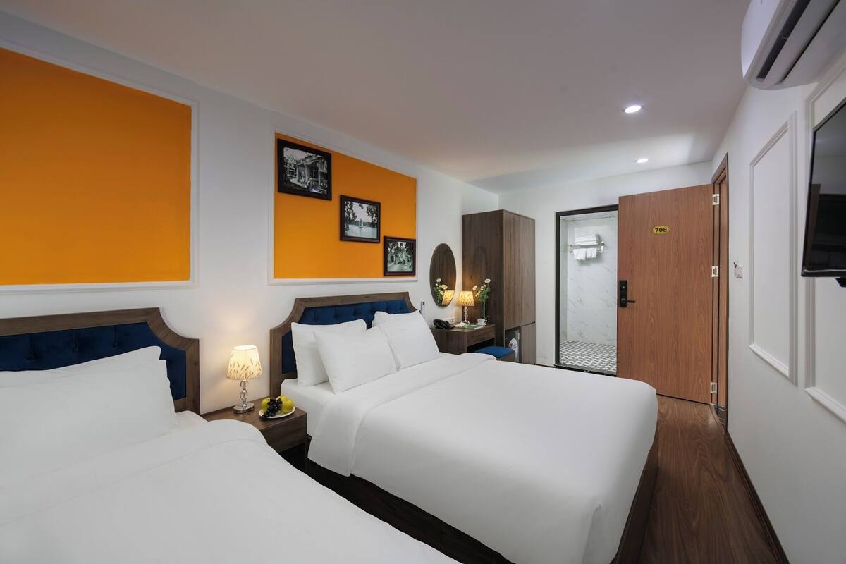 A hotel room with two beds, a wooden wardrobe, a mirror, and a door with a number.