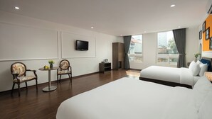 Ein Hotelzimmer mit einem großen Bett, zwei Sesseln, einem kleinen Tisch mit einer Vase, einem flachbildfernseher an der Wand und einem Fenster mit Vorhängen.