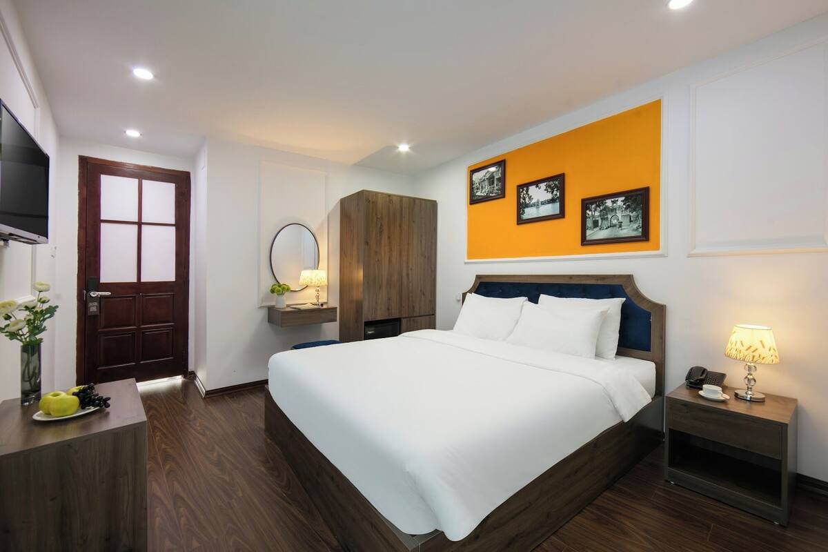 A hotel room with a large bed, a wooden wardrobe, a bedside table with a lamp, and a wall-mounted TV.