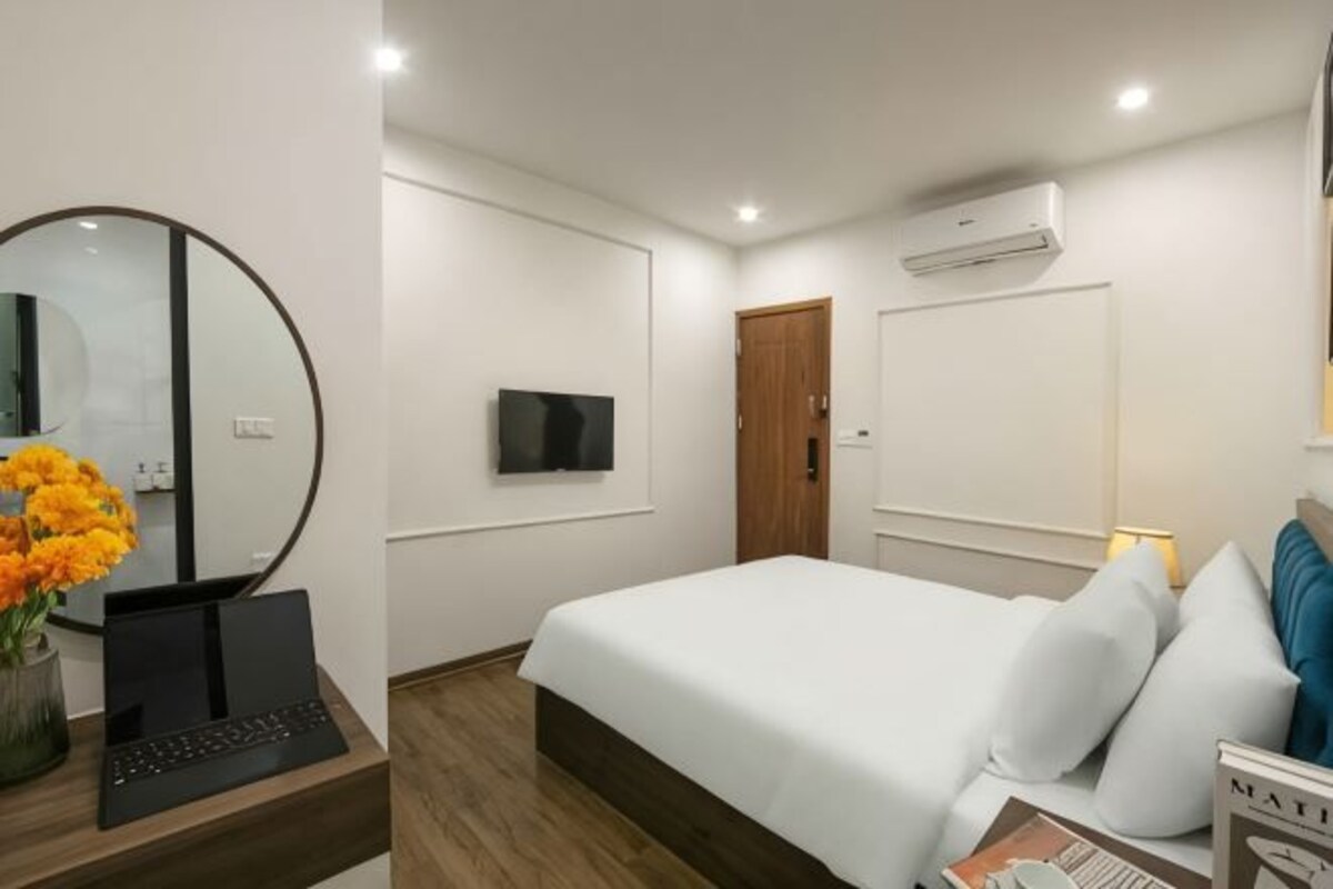 A hotel room with a bed, a TV, a mirror, and a laptop on a desk.