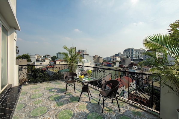 A balcony with a patterned floor, two wicker chairs, a small table with a vase, and a view of a cityscape. - Dream Premium Hotel & Spa (Hanoi)