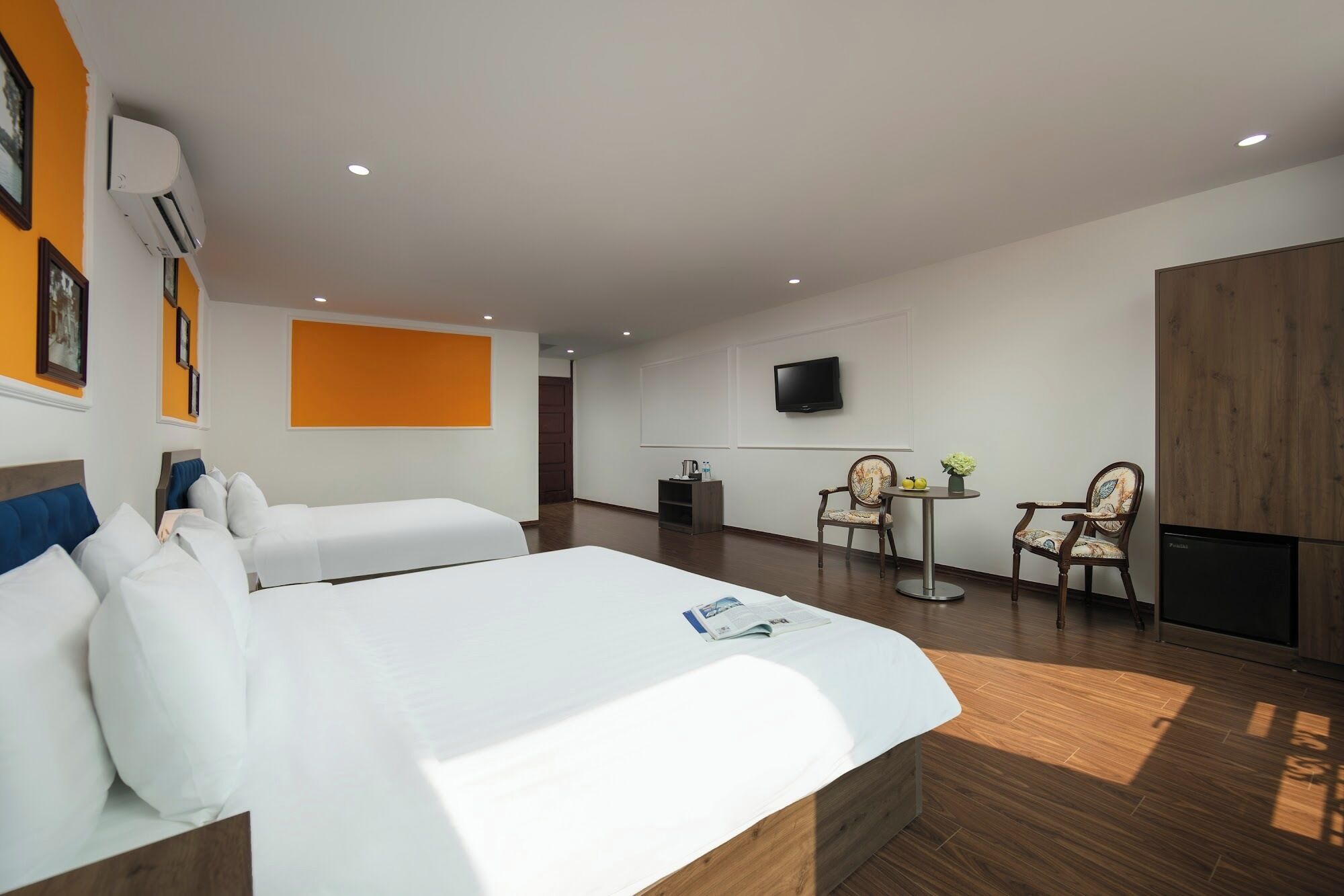 Una habitación de hotel con dos camas, televisor, una mesita con sillas y un equipo de aire acondicionado.
