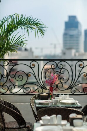 A dining table with white tableware and a vase with pink flowers, set against a balcony railing with a cityscape in the background. - Dream Premium Hotel & Spa (Hanoi)