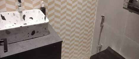 Un baño con un lavamanos blanco, un mueble negro, una ducha con puerta blanca y un suelo estampado.