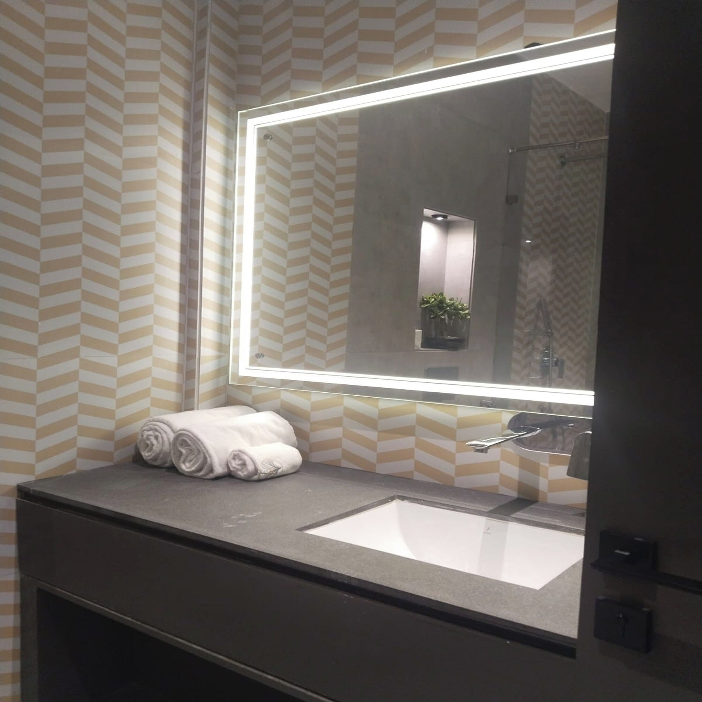 A bathroom with a large mirror, a sink, and two rolled towels on the counter.