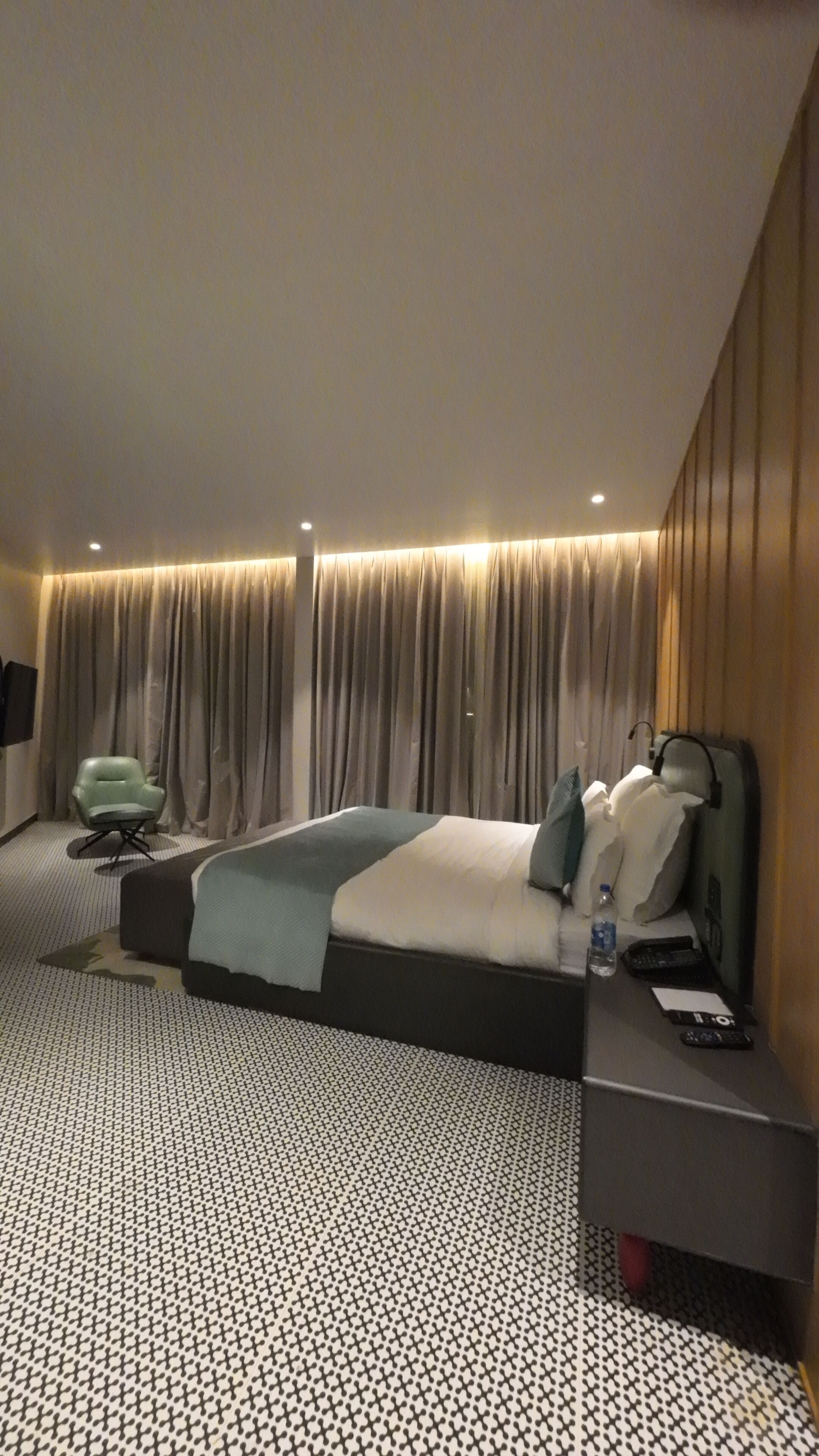 A modern hotel room with a bed, a desk, a chair, and a large window with curtains.