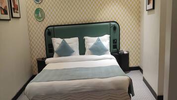 A hotel room with a bed, a nightstand, a wall clock, and framed artwork on the wall.