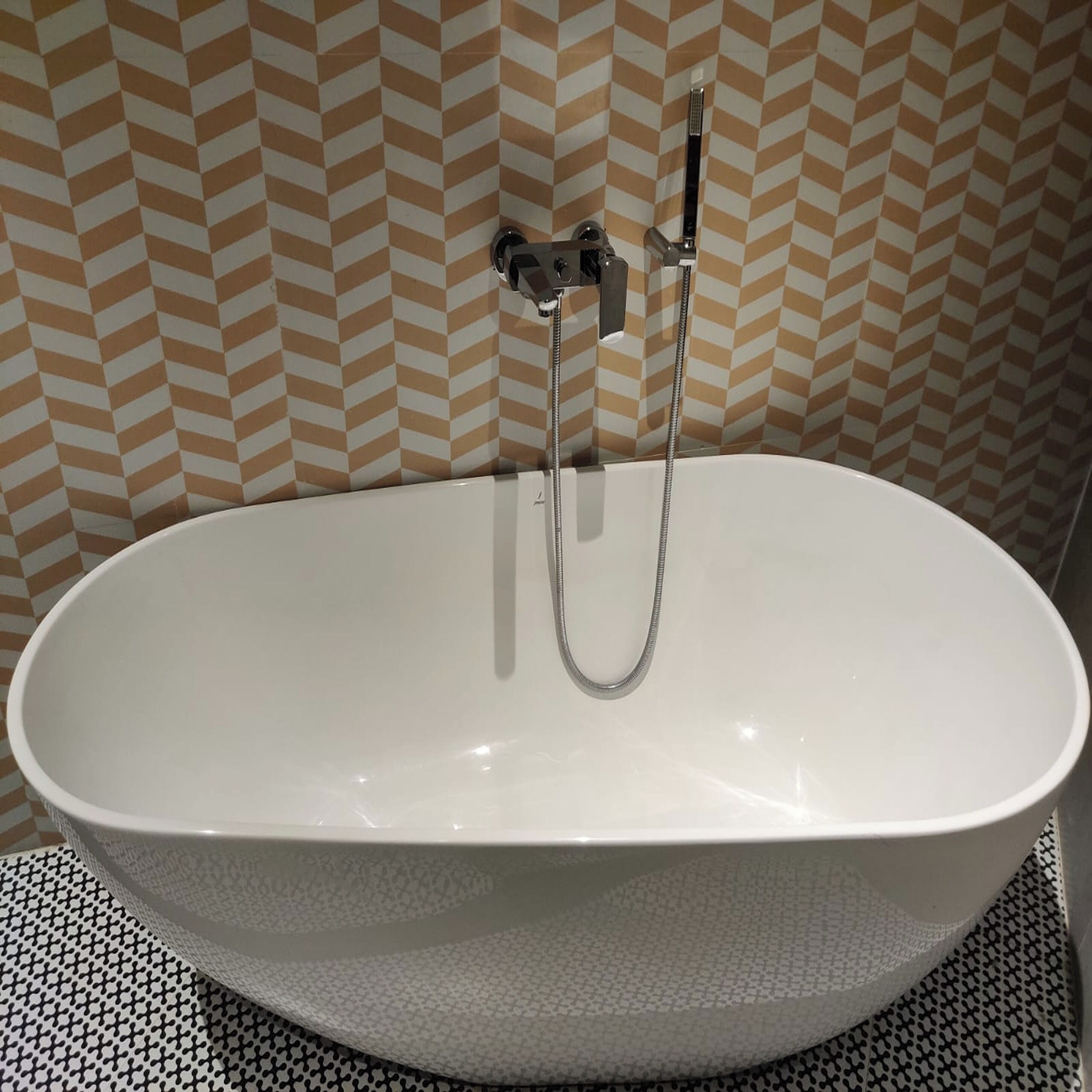 A white oval bathtub with a handheld showerhead, set against a chevron-patterned wall.