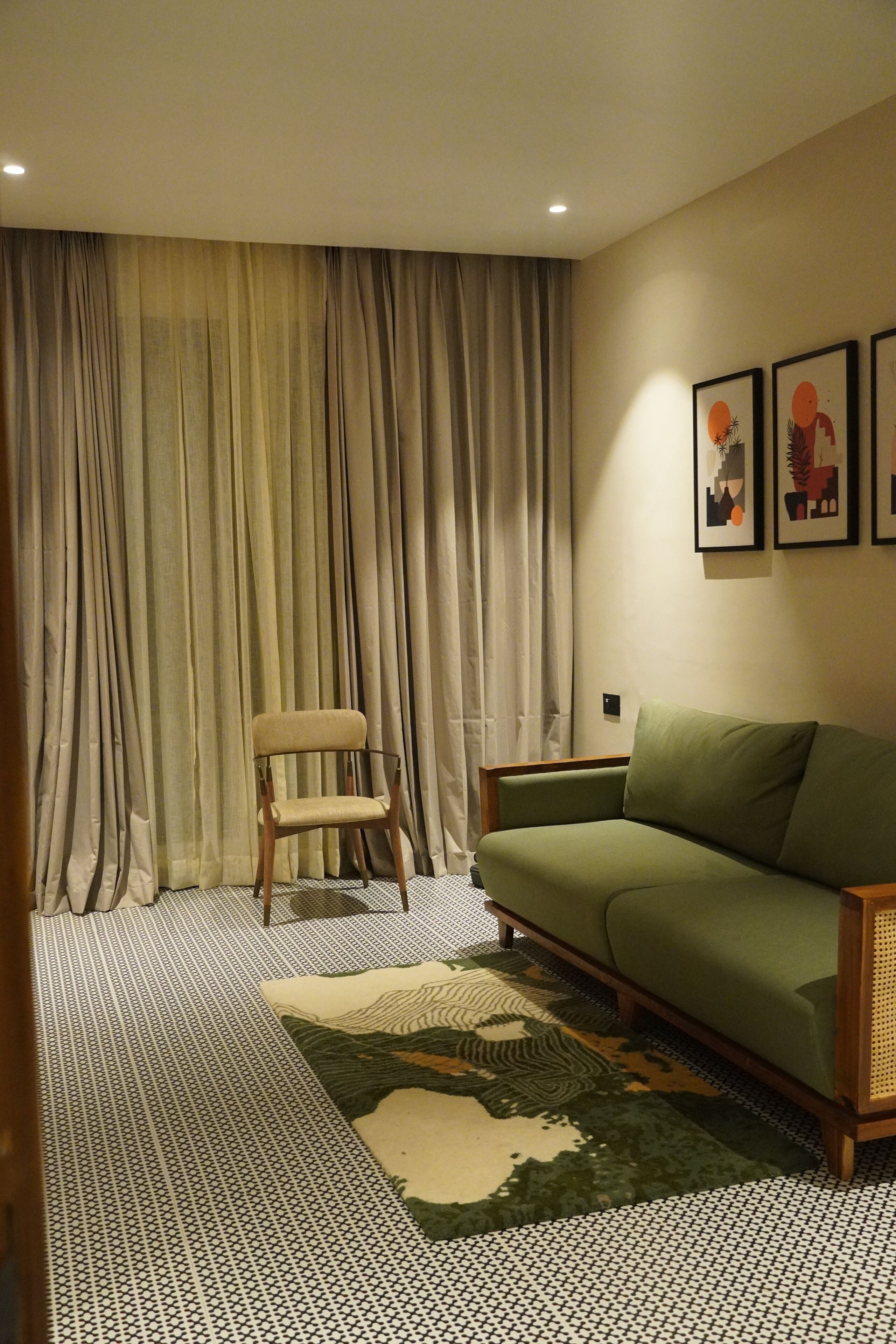 Un salon avec un canapé vert, un tapis à motifs, une chaise en bois et une grande fenêtre avec des rideaux.