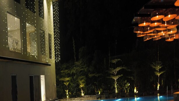 Ein Schwimmbecken bei Nacht mit klarem Wasser, umgeben von Bäumen und einem Gebäude mit beleuchteten Fenstern.