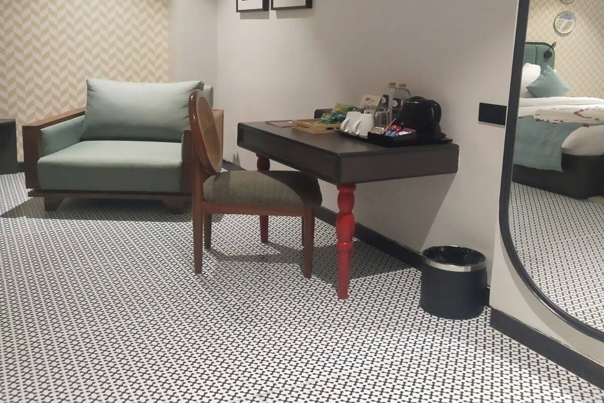 Habitación de hotel con sofá, escritorio y silla, cama, espejo y suelo estampado.