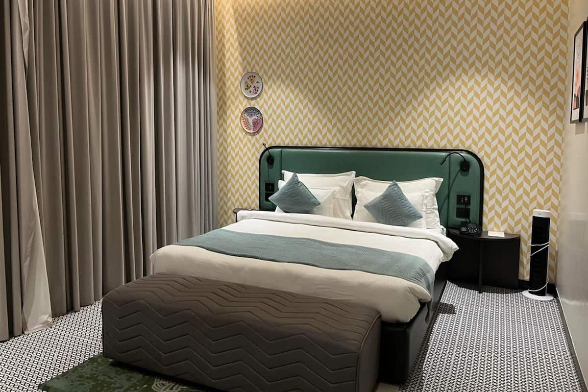 Habitación de hotel con cama, mesita de noche, lámpara y pared con diseño en zigzag.