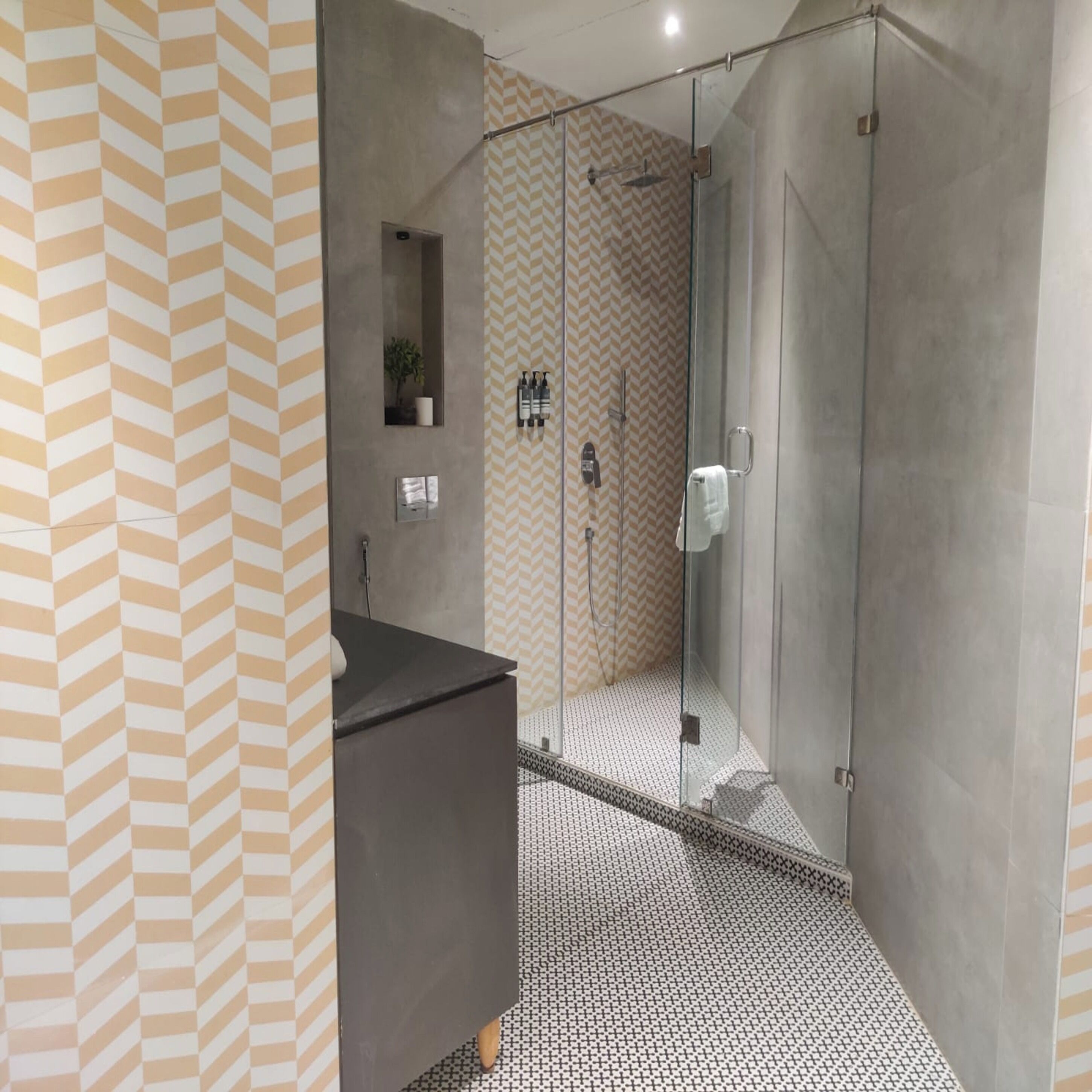 A modern bathroom with a glass shower enclosure, a sink with a mirror, and a patterned floor.