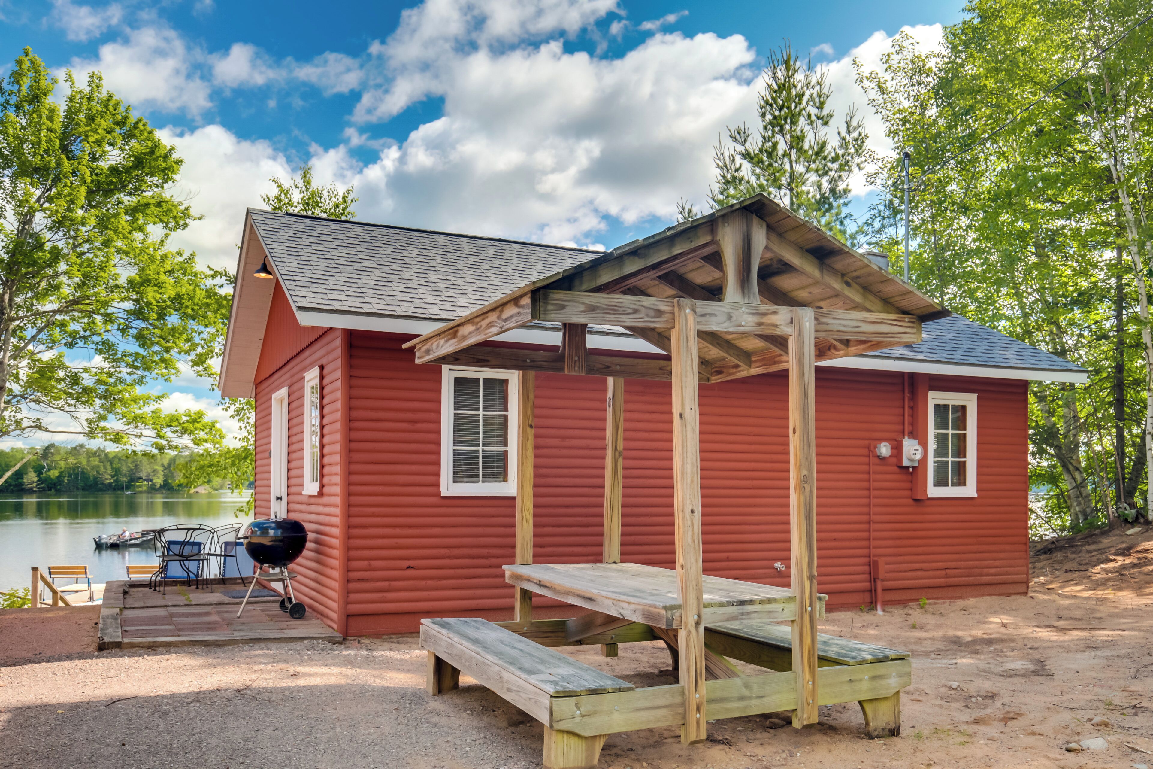 A red cabin with a wooden deck, a grill, and a table.