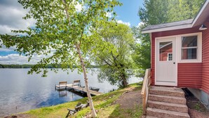 A cabin with a dock extending into a calm lake, surrounded by trees and a clear sky. - Private Dock & Rowboat! Cabin on Bearskin Lake (Harshaw)