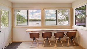 A room with a large window overlooking a lake, a wooden desk, and four chairs. - Private Dock & Rowboat! Cabin on Bearskin Lake (Harshaw)
