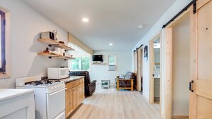A modern kitchen with white appliances, wooden cabinets, and a TV mounted above the counter. - Private Dock & Rowboat! Cabin on Bearskin Lake (Harshaw)