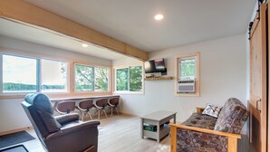 A spacious living area with a leather sofa, a patterned armchair, a TV mounted on the wall, and a small table. - Private Dock & Rowboat! Cabin on Bearskin Lake (Harshaw)