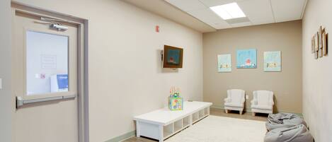 A room with a white bench, a white carpet, and two white chairs.