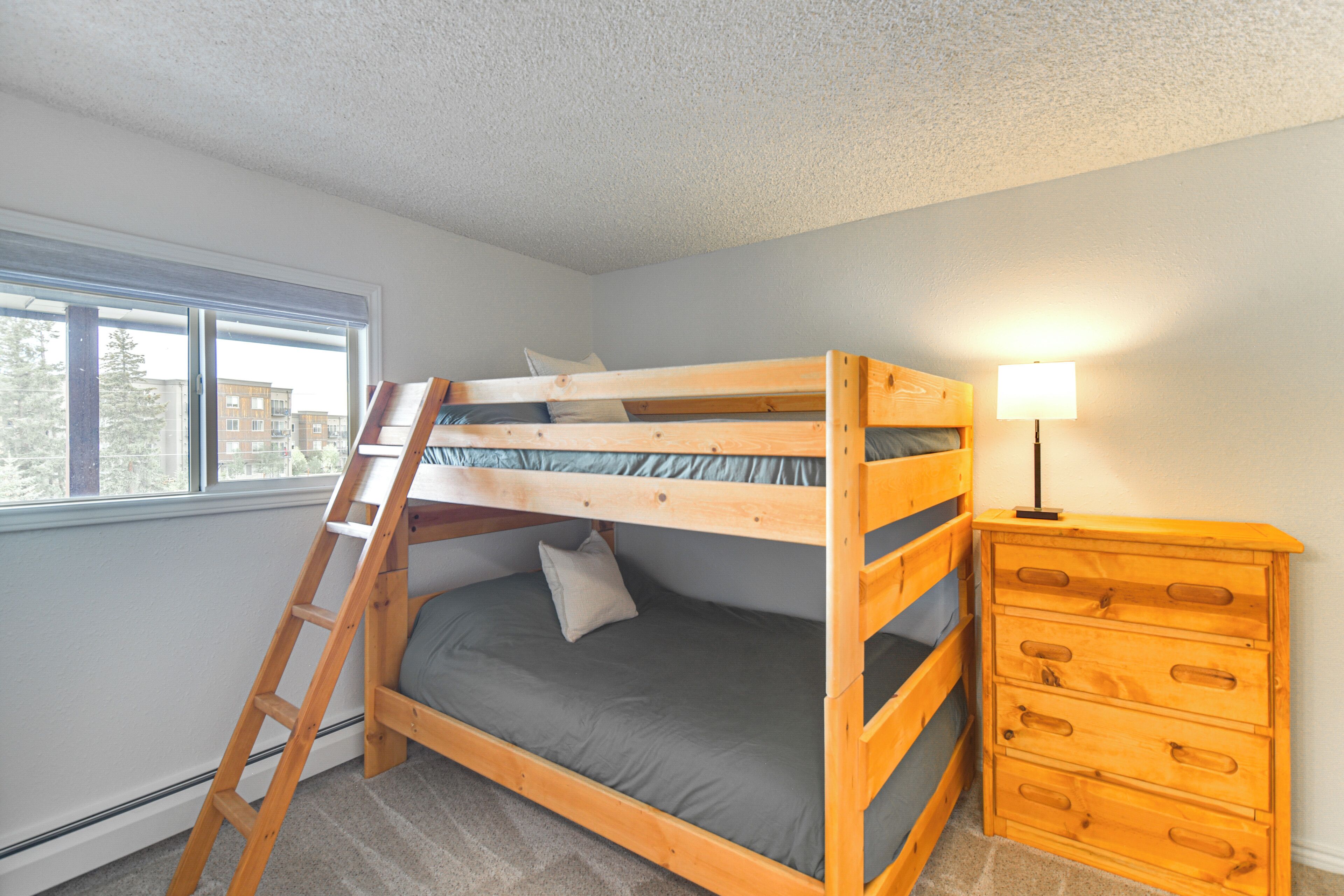 A bunk bed with a ladder, a dresser, and a window with a view of buildings.