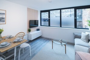 Enjoy a spacious living area with a large window offering a view of the outdoor space, a flat-screen TV, and a dining table.