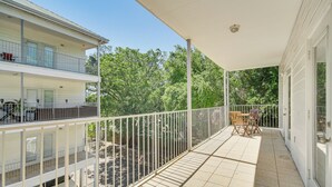 Ein überdachter Balkon mit Fliesenboden, weißen Geländern und Blick auf eine von Bäumen gesäumte Straße.