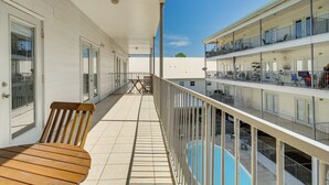 Ein Balkon mit Holztisch und -stühlen, ein Schwimmbad und ein weißes Gebäude im Hintergrund mit mehreren Balkonen.