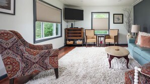 A living room with a patterned sofa, a blue couch, a white shag carpet, a wooden cabinet, a TV, and two chairs.