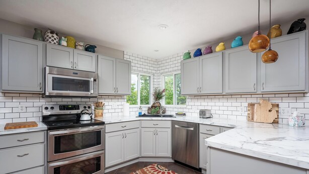 A kitchen with white cabinets, a microwave, a stove, a dishwasher, and a window with a view of greenery.