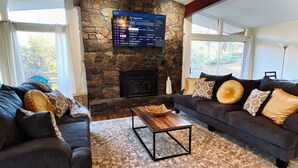 A living room with a stone fireplace, two sofas with patterned cushions, and a flat-screen TV mounted on the wall. - Spa, 5 minutes from Sequoia National Park. Spacious, convenient and private. (Three Rivers)