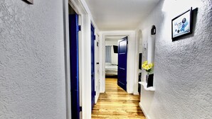 Un pasillo con suelo de madera, puertas azules y una pared blanca con textura.