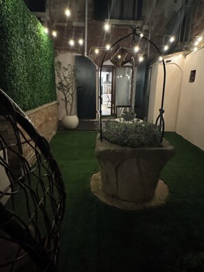 Stroll through the serene garden, surrounded by lush greenery and a central potted plant arrangement, leading to a charming doorway.