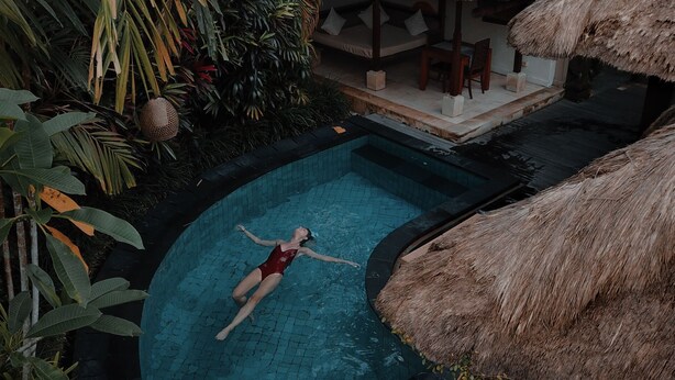 A person floating in a pool surrounded by tropical plants and a thatched roof structure. - HOTEL ARAB INN (Mohali)