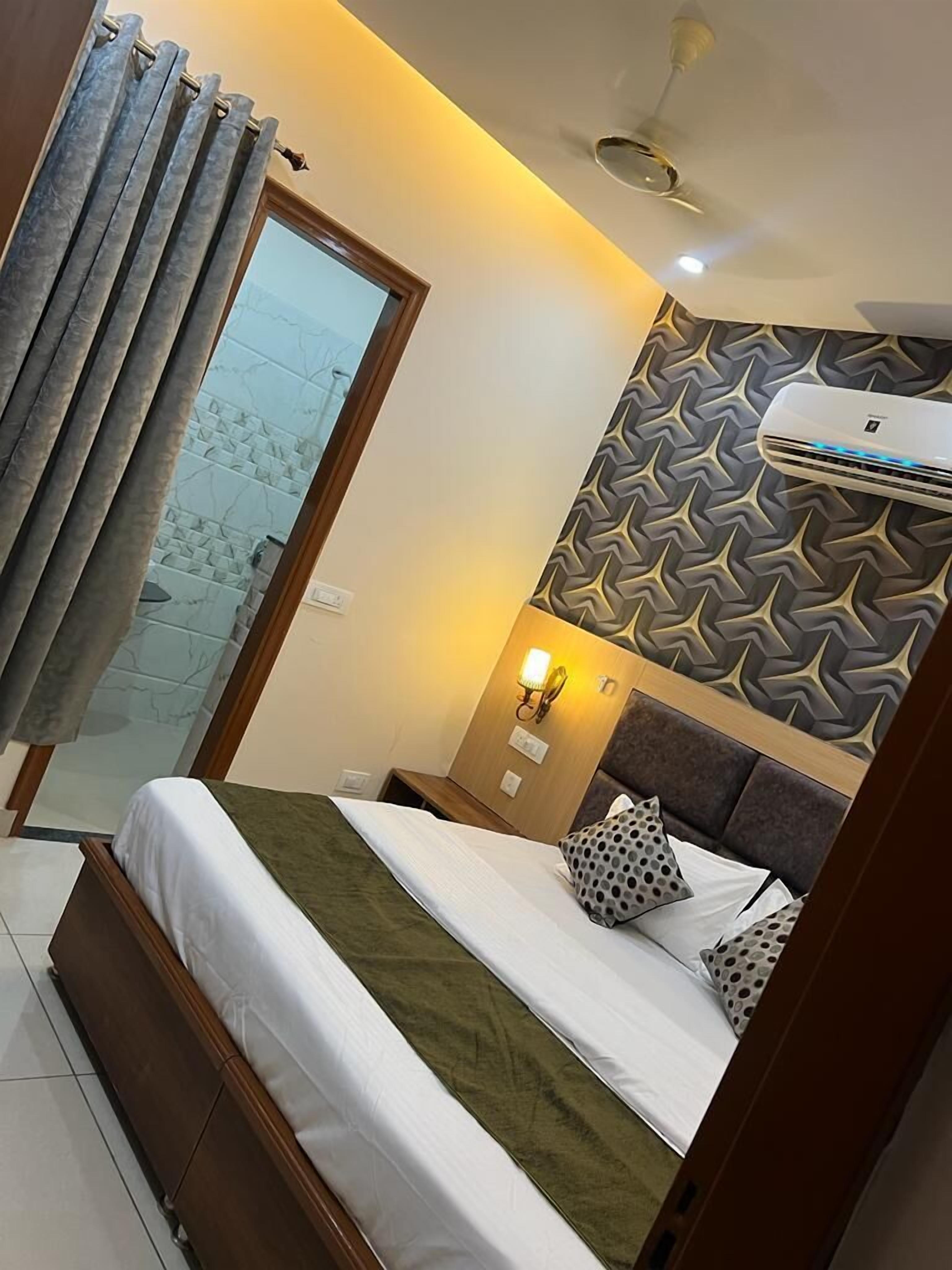 Habitación de hotel con cama, aire acondicionado de pared, mesita de noche con lámpara y pared con diseño.