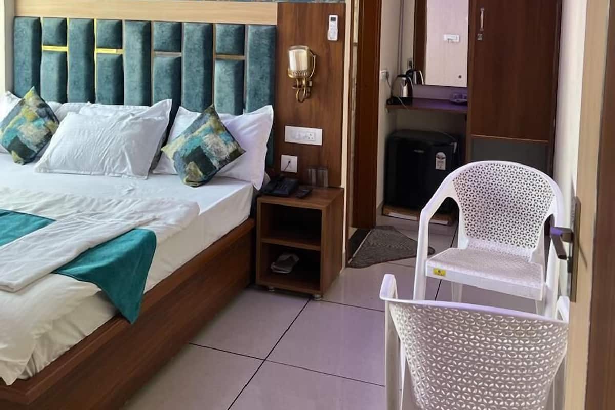 Une chambre d’hôtel avec un lit, une table de chevet, une chaise, un bureau et une salle de bain visible à travers une porte ouverte.