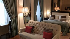 A hotel room with a large bed, a sofa with red cushions, a side table, and a mirror. - HOTEL ARAB INN (Mohali)
