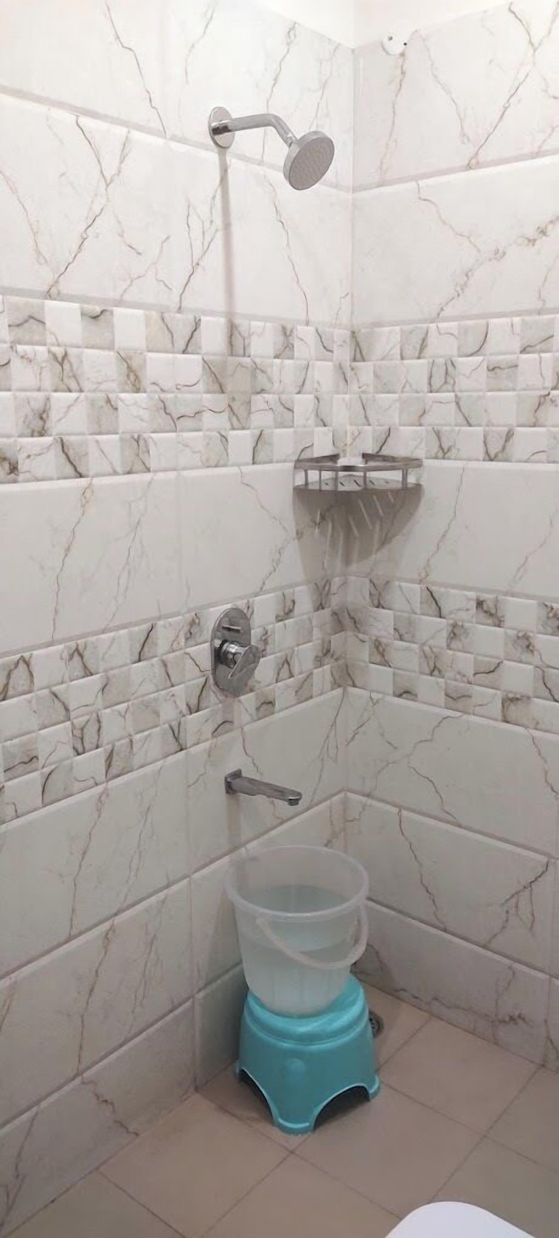 A bathroom with white marble tiles, a showerhead, a toilet, and a blue plastic container.