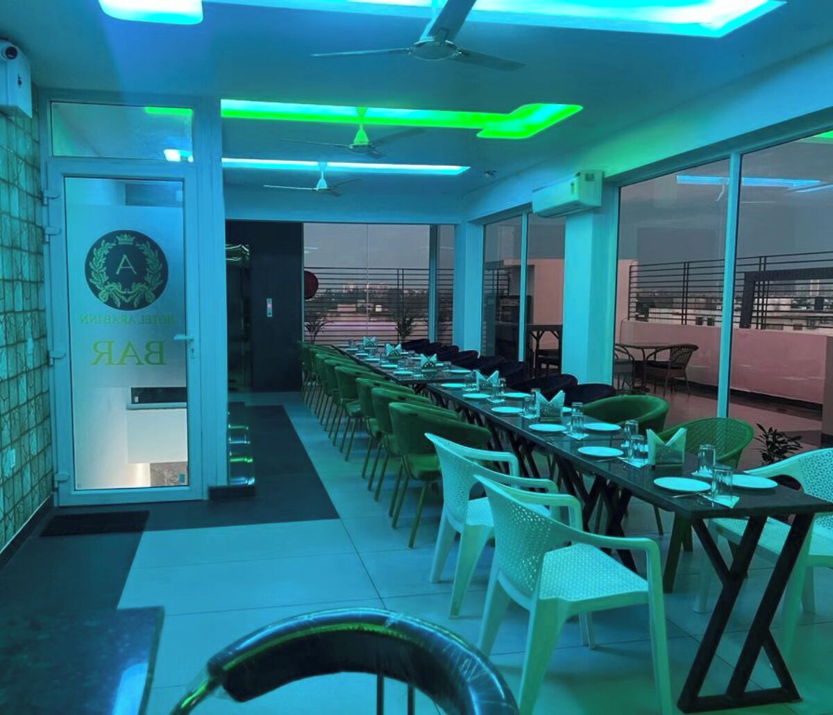 A restaurant with a long dining table, chairs, and a view through large windows.