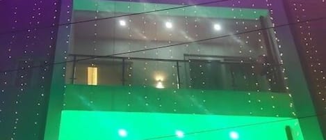 A hotel with multiple floors, illuminated by colorful lights. The sign indicates it is a hotel with rooms available for booking.