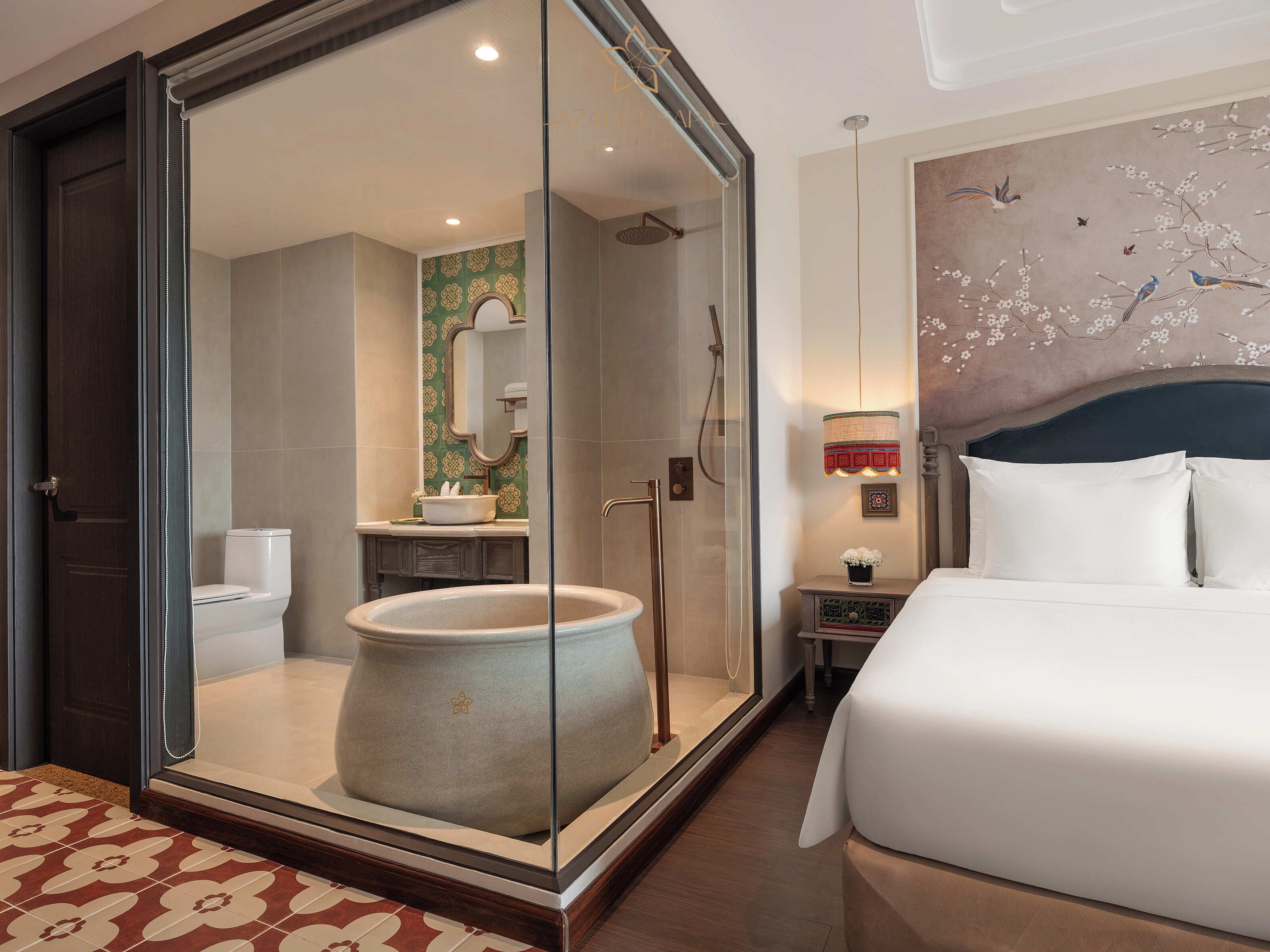 A hotel room with a large bed, a glass-enclosed shower, a bathroom with a toilet and sink, and a decorative wall mural.