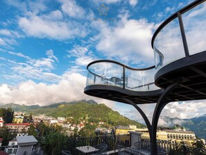 A balcony with a glass enclosure overlooking a town and mountains. - Azalea Sapa Hotel (Sa Pa)