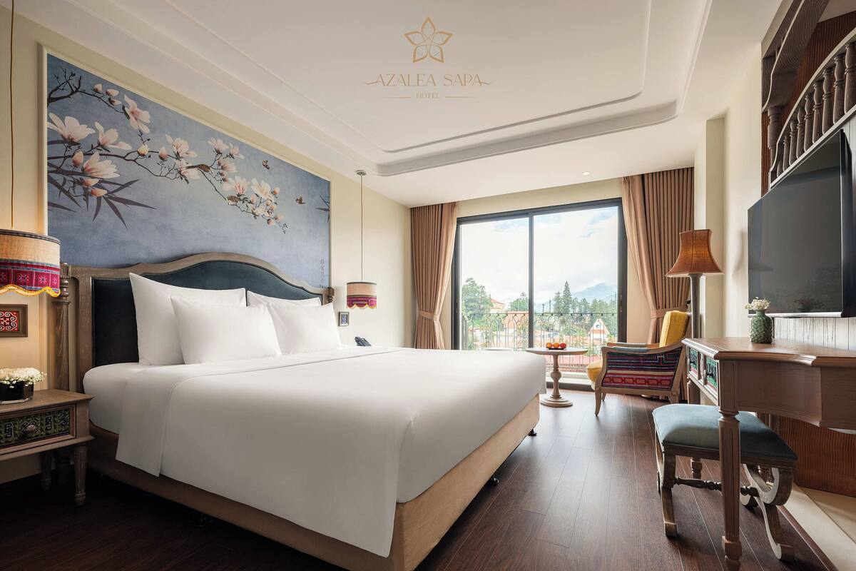 A hotel room with a large bed, a desk, a chair, a TV, and a view of the city.