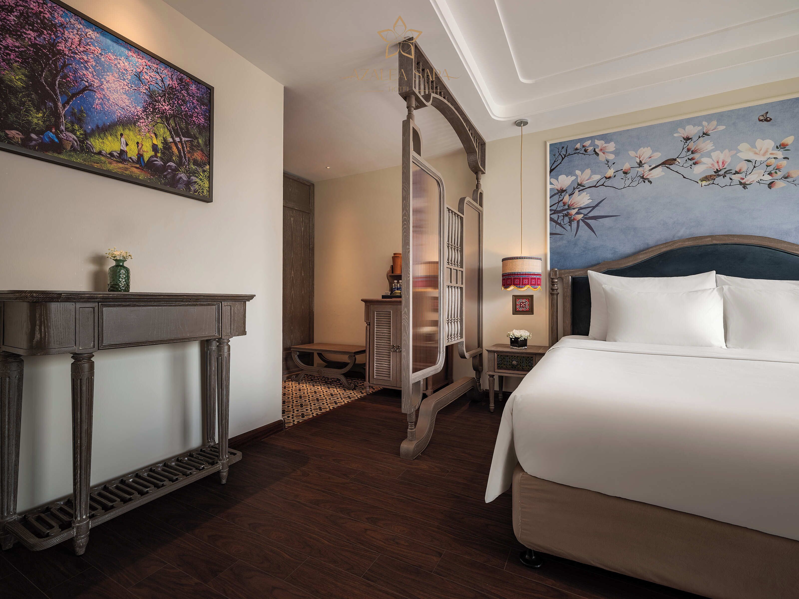 A hotel room with a large bed, a wooden console table, a mirror, and a painting of cherry blossoms.