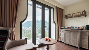Habitación de hotel con balcón, una mesa de comedor con fruta, un sofá y un mueble con utensilios de cocina.