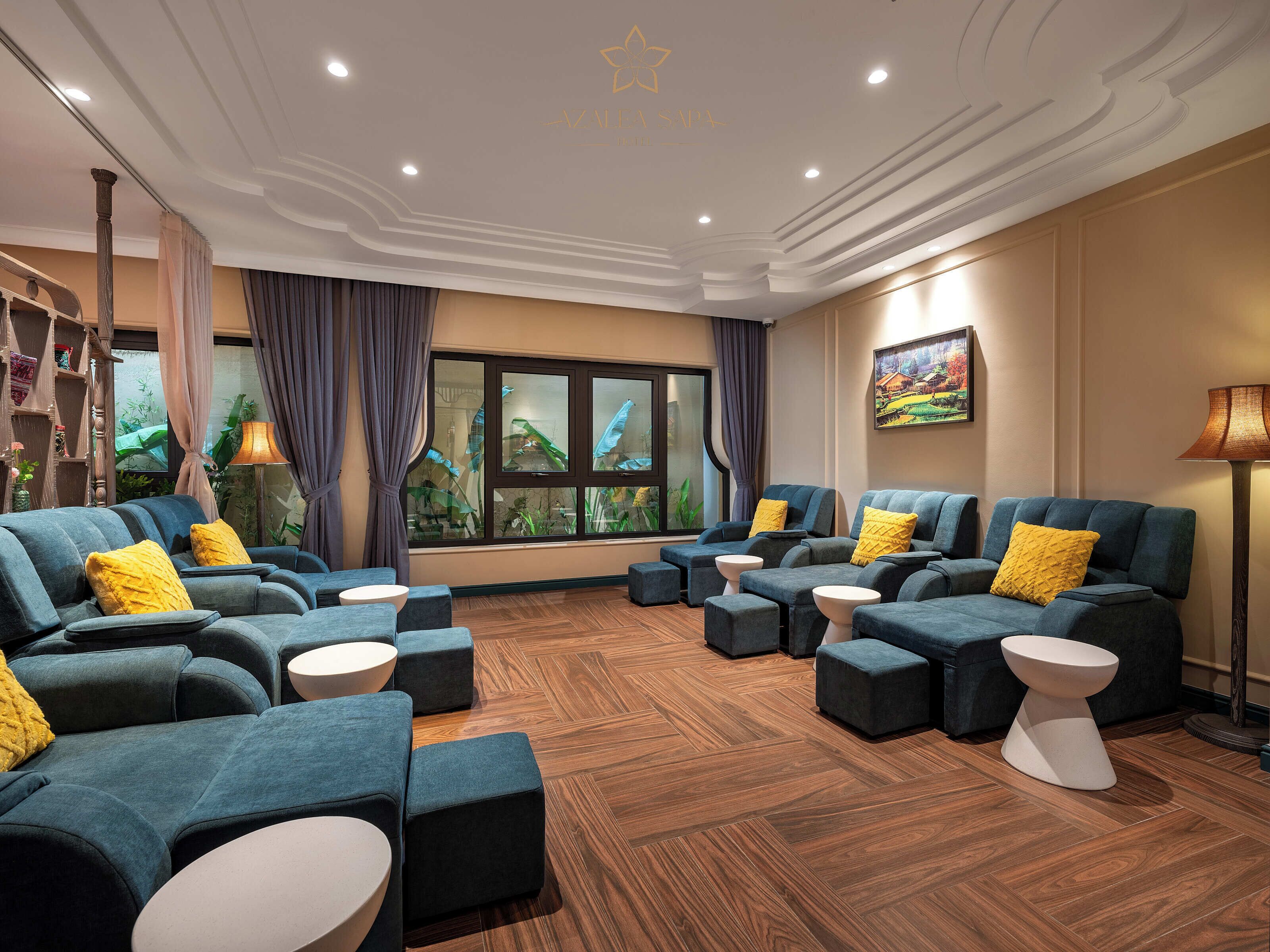 A modern spa room with multiple seating areas, a large window with curtains, and a wooden floor.