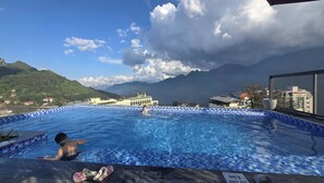 Una piscina con borde de azulejos, una persona en el agua y un paisaje montañoso al fondo.