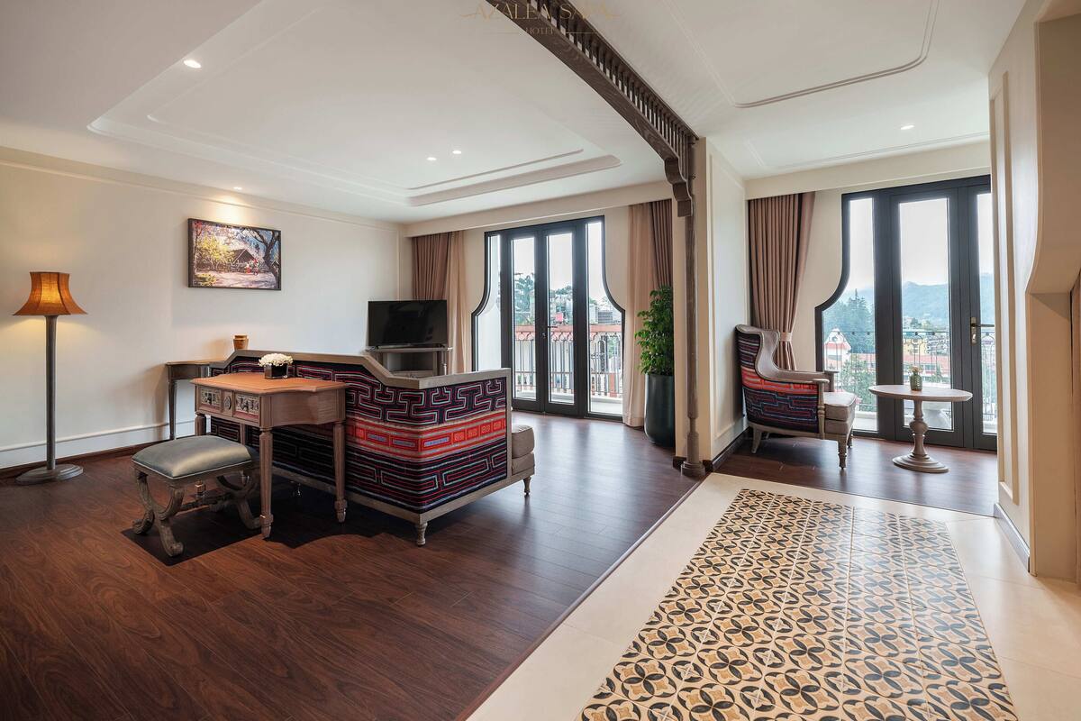 A spacious living room with a wooden floor, a sofa, a TV, a desk, and a large window offering a city view.