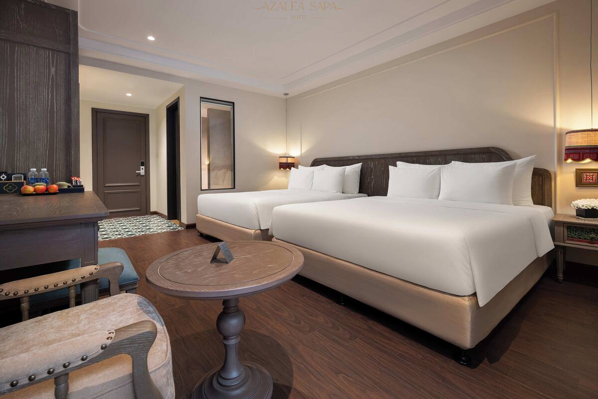 A hotel room with a large bed, a smaller bed, a desk with a chair, a round table, and a mirror.